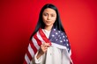 Young beautiful chinese woman wearing United States flag over isolated red background with a confident expression on smart face thinking serious