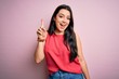 © Krakenimages.com - Young brunette woman wearing casual summer shirt over pink isolated background pointing finger up with successful idea. Exited and happy. Number one.