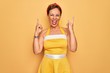 © Krakenimages.com - Middle age senior pin up woman wearing 50s style retro dress over yellow background shouting with crazy expression doing rock symbol with hands up. Music star. Heavy music concept.