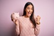 © Krakenimages.com - Young beautiful brunette woman holding piggy bank saving money for retirement screaming proud and celebrating victory and success very excited, cheering emotion