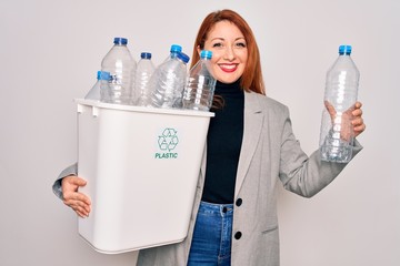 Poster - Young beautiful redhead woman recycling holding trash can with plastic bottles to recycle with a happy face standing and smiling with a confident smile showing teeth