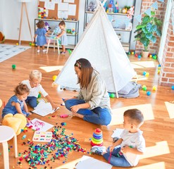 Poster - Beautiful teacher and group of toddlers playing around lots of toys at kindergarten