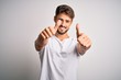 © Krakenimages.com - Young handsome man with beard wearing casual t-shirt standing over white background approving doing positive gesture with hand, thumbs up smiling and happy for success. Winner gesture.