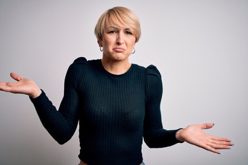 Sticker - Young beautiful blonde woman with modern short hair hairstyle standing over isolated background clueless and confused expression with arms and hands raised. Doubt concept.