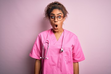 Poster - African american nurse girl wearing medical uniform and stethoscope over pink background afraid and shocked with surprise expression, fear and excited face.