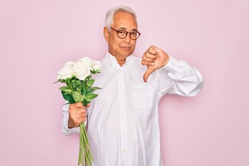 Canvas Print - Middle age senior grey-haired man holding romantic bouquet of white roses over pink background with angry face, negative sign showing dislike with thumbs down, rejection concept