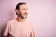 © Krakenimages.com - Middle age hoary man wearing casual t-shirt standing over isolated pink background looking away to side with smile on face, natural expression. Laughing confident.