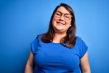 Beautiful brunette plus size woman wearing casual t-shirt over isolated blue background with a happy and cool smile on face. Lucky person.