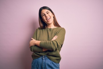 Young beautiful woman wearing casual sweater standing over isolated pink background happy face smiling with crossed arms looking at the camera. Positive person.