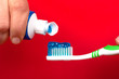 hand squeezes toothpaste on a toothbrush on a red background close-up. caries prevention and oral care