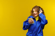 © YURII MASLAK - Enjoy listening to music. Beautiful young curly-haired woman with headphones listening music,singing and dancing. Funny emotional smiling girl with earphones and mobile phone on yellow background.