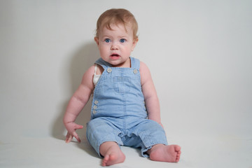 Wall Mural -  emotional portrait of a one-year-old baby in denim overalls on a uniform light background