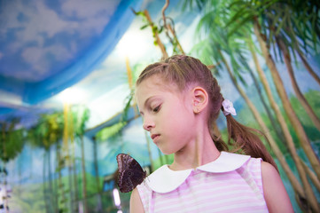 educational process of interested little girl looking at butterfly insect sitting on her shoulder in insectarium