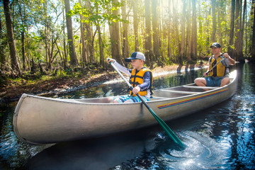 adventuresome father and son canoeing together on a beautiful river in a thick forest. family vacati