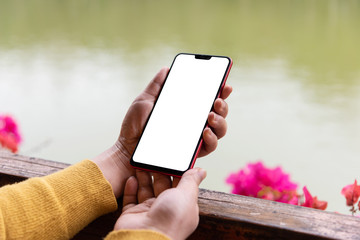 Wall Mural - Close-up of female holding blank smartphone on park pond background