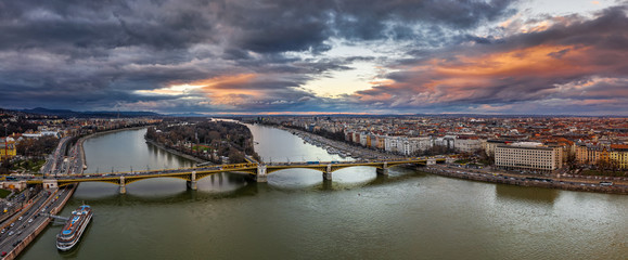 Wall Mural - Budapest, Hungary - Aerial panoramic drone view of Margaret Bridge (Margit Hid) and Margaret Island (Margit-sziget) with a spectacular golden sunset and sky above. Yellow trams going on the bridge