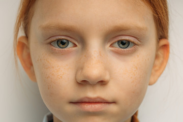 close-up portrait of serious confident caucasian child girl with long red hair and big blue eyes isolated over white background. natural red haired girl with freckles confidently look at camera