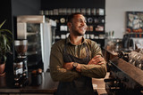 Fototapeta  - Young afro-american small coffee shop owner standing behind counter wearing apron with crossed arms looking away