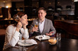 © Roman - bored caucasian woman with champagne and handsome man entertaining her. male in love with her, while woman is not interested in rendezvous with him. in luxury restaurant