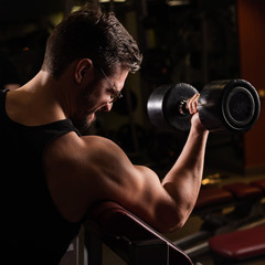 A handsome man with glasses doing an exercise for biceps with a barbell. The guy is engaged in bodybuilding. Trainer in the gym with muscular arms.