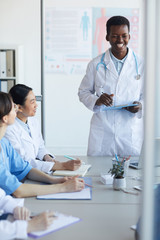 Wall Mural - Portrait of young African-American doctor giving speech while standing at table during medical council or conference in clinic, copy space