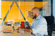 © Nana_studio - Have a nice working day. Confident young african american businessman working on laptop and talking on cell phone while sitting at his workplace in office