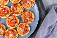 Small Mini Pizzas Topped With Cheese, Tomato, Yellow And Red Bell Peppers And Salami Sausage On Gray Plate