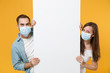 People in sterile face masks hold big white empty blank billboard isolated on yellow background studio. Epidemic rapidly spreading coronavirus 2019-ncov medicine flu virus ill sick treatment concept.