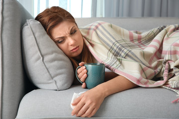 Wall Mural - Sick woman with cup of hot drink lying on sofa at home. Influenza virus