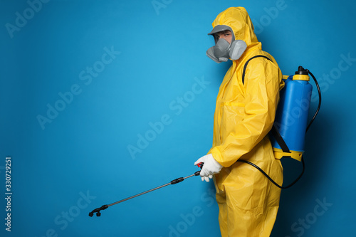Cuadros en Lienzo Man wearing protective suit with insecticide sprayer on blue background, space for text