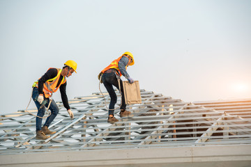Poster - Construction worker wearing safety harness belt during working on roof structure of building on construction site,Roofer using air or pneumatic nail gun and installing concrete roof tile on top roof.