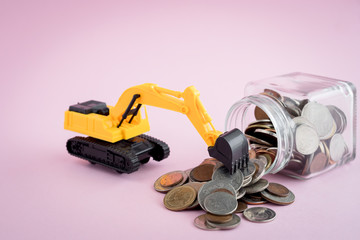 The excavator loader model with pile of coins in the glass jar on pink background for saving money, investment, business and finance concept