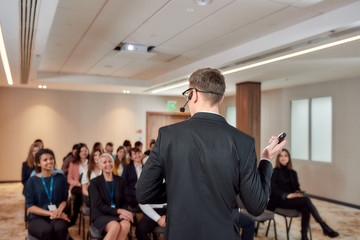 Next Generation Leadership. Young male speaker with headset and laser pointer giving a talk at corporate business training conference. Audience in the background