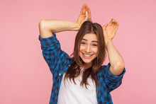 I Am Rabbit! Portrait Of Amazing Playful Pretty Girl In Checkered Shirt Showing Bunny Ears Gesture, Laughing And Having Fun, Childish Carefree Mood. Indoor Studio Shot Isolated On Pink Background