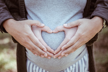 Cropped image of lovely couple do hand sign a heart shape and hugging the tummy. Conceptual of couple expecting a baby with love.