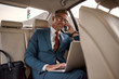 © Svitlana - Staying connected. Cheerful mature businessman in full suit working on his laptop and talking on the phone with client and smiling while sitting in the car
