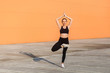 © khosrork - Slim fit woman in tight sportswear, black pants and top, practicing yoga, standing in Vrikshasana tree pose and meditating, doing balancing asana with hands up. Health care, sport activity outdoor