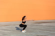 © khosrork - Fit young woman in tight sportswear, black pants and top, practicing outdoor, doing split or lunge squat exercise with stretched out hands, lower-body exercise. Health care concept, sport activity