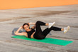 © khosrork - Fit sporty beautiful girl in tight sportswear, black pants and top, lying on mat doing sit ups, crunch exercise, training abdominal muscles. Health care and weight loss concept, sport activity outdoor