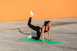 © khosrork - Attractive fit brunette woman in tight sportswear, black pants and top, practicing yoga, doing one legged plank pose bow leg, training muscles and flexibility. Health care, sport activity outdoor