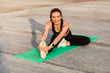 © khosrork - Cheerful smiling athletic woman in tight sportswear, black pants and top, practicing yoga, doing Head-to-Knee Pose, touching toes, stretching leg and back muscles. Health care, sport activity outdoor