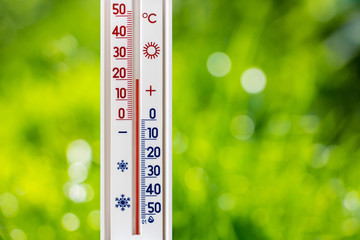 A thermometer on a blurred background of green grass shows 20 degrees of heat_