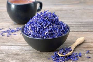 Wall Mural - Black ceramic bowl of dry blue cornflowers petals and herbal tea cup on table. Herbal medicine.