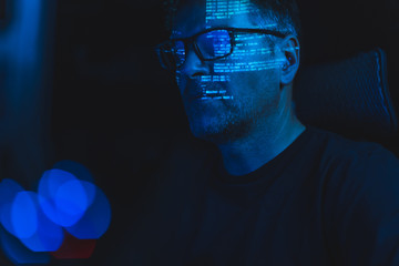 close-up of middle aged caucasian man with glasses sitting and watching computer screen in the dark