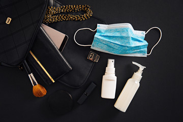 Top view of women purse accessorize, with protective face mask and hand sanitizer inside it.  