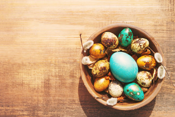 Wall Mural - Bright easter eggs in a clay bowl and fluffy willow branches on a old wooden background, top view. Easter background.	