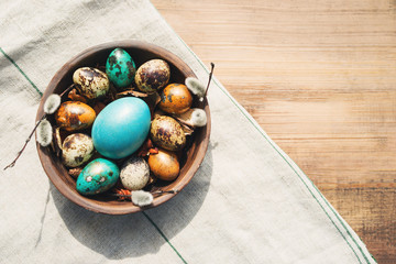 Wall Mural - Bright easter eggs in a clay bowl and fluffy willow branches on a old wooden background, top view. Easter background.	