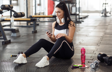 Wall Mural - Young lady with mobile phone and headphones in sports club