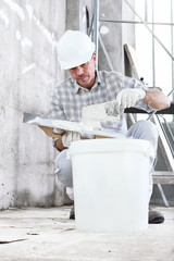 Wall Mural - plasterer man at work, take the mortar from the bucket to plastering the wall of interior construction site wear helmet and protective gloves, and scaffolding on background