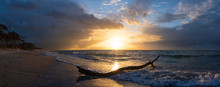 Beautiful Sunset Over The Sea, Panorama View Of A Dramatic Sunset With Dark Clouds. Rain Clouds Or Storm Clouds Before The Storm, Tree Trunk Lies In The Water On The Beach